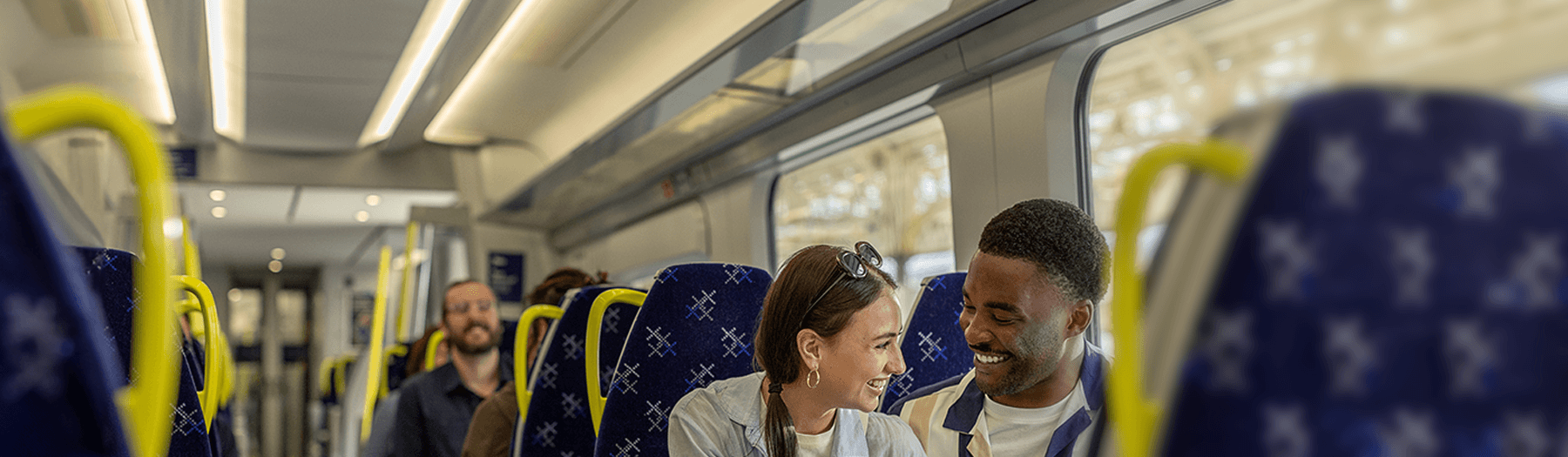 Male and female travelling on a ScotRail train smiling at each other. 